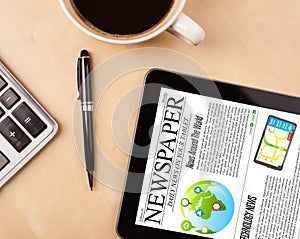 Tablet pc shows news on screen with a cup of coffee on a desk