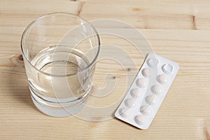 Tablet pills blister and a  glass of water rest on a wooden table with copy space for your text