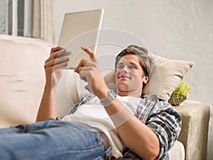 Tablet, relax and man on sofa in home for social media, networking and browse website. Happy, smile and person lying on