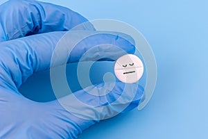 Tablet with a sleeping smiley in a hand in a medical glove on a blue background. Sleeping pills for insomnia