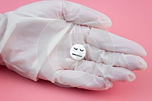 Tablet with a sleeping smiley in a hand in a medical glove on a pink background. Sleeping pills for insomnia