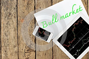 Tablet, smartphone and paper with text bull market on wood table