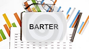 The tablet with text BARTER on business charts,glasses and pen