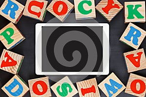 Tablet touchpad with colorful alphabet wooden blocks on black background. Flat lay