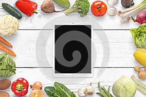 Tablet and vegetables on wihite wooden desk. Top view