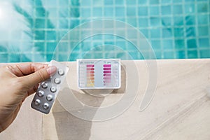 Tablet for water testing in girl hand over pooltester test kit on swimming pool edge background