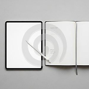 Tablet with a white stylus is placed next to an open notebook on a