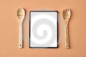 Tablet, wooden fork and spoon isolated on beige background, conceptual photography for food blog or advertising