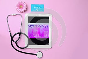 Tablet with word GYNECOLOGY, business card, flower and stethoscope on pink background, flat lay