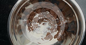 TABLETOP slowmotion shot: chef chocolatier adds hot milk to the metal bowl with shunks of milk and dark chocolate, raw