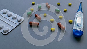 Tablets, caplets and thermometer on light gray background, yellow, green and orange pills on top right corner of the
