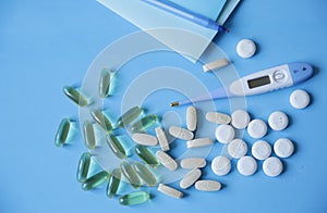 tablets, capsules and an electronic thermometer for measuring body temperature, a notebook and a pen on a blue background, with c