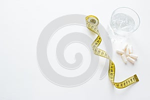 Tablets in capsules, a glass of water and a measuring tape concept diet with copy space on a white background