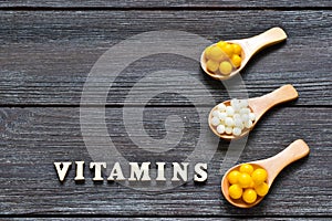 Tablets and capsules in wooden spoons with the inscription Vitamins on a wooden background. Copy space. Vitamins, prebiotics, prob photo
