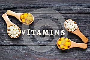 Tablets and capsules in wooden spoons with the inscription Vitamins on a wooden background. Copy space. Vitamins, prebiotics, prob photo
