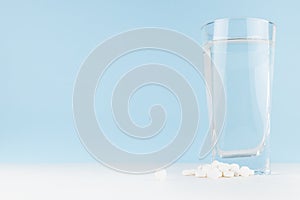 Tablets and glass of water on white table and blue wall - medical and pharmacy remedies for health and prevent, therapy disease.
