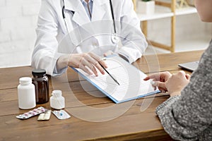 Tablets and medication to patient. Adult woman doctor in white coat shows to put signature in tablet on wooden table