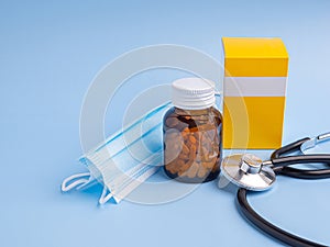 Tablets medicine in a bottle and a box with a stethoscope and mask on a light blue background.