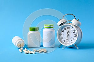 Tablets and pills with cans of medicines next to an alarm clock on a blue background.