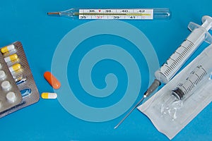 Tablets, syringes and a medical thermometer on a blue background