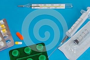 Tablets, syringes and a medical thermometer on a blue background