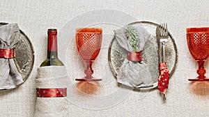 Tableware for Christmas or Xmas festive dinner, linen napkin on plate, knife, fork, red wine glass, bottle of wine on