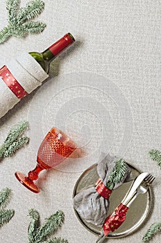 Tableware for Christmas or Xmas festive dinner, linen napkin on plate, knife, fork, red wine glass, bottle of wine on