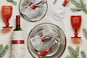 Tableware for Christmas or Xmas festive dinner, linen napkin on plate, red wine glass, bottle of wine on rustic