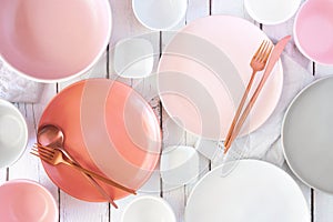 Tableware set in pastel pink, coral, white and grey colors. Above view on white wood.