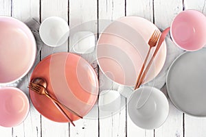 Tableware set in pastel pink, coral, white and grey. Top view on white wood.