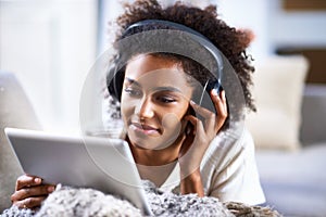 Tabs are so versitile. a young woman using a digital tablet and wearing headphones while relaxing at home.