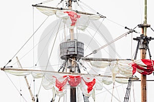 Tackles of an old sailing vessel - a mast, a mast, raised red-white sails, ropes.