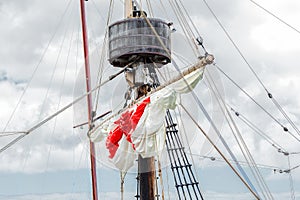 Tackles of an old sailing vessel - a mast, a mast, raised red-white sails, ropes.