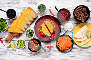 Taco bar table scene with a variety of ingredients on a rustic white wood background