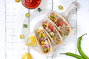 Taco - wheat tortilla with meat, vegetables, corn, greens. Delicious mexican snack on a white wooden background.