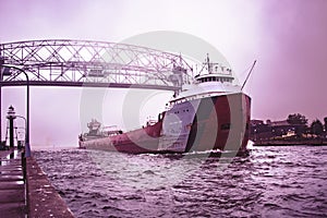 Taconite-loaded freighter/container ship passing under aerial lift bridge