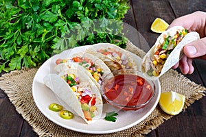 Tacos - wheat tortilla with meat, vegetables, greens and corn with tomato sauce on a dark wooden background.