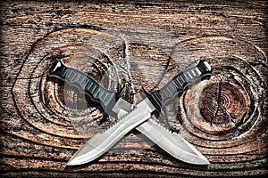 Tactical Combat Hunting Survival Bowie Knives With Crossed Blades On Grunge Vignetted Old Knotted Pinewood Grunge Background photo