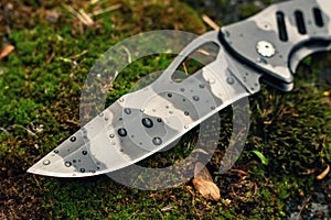 Tactical folding knife with water drops for survival on moss background