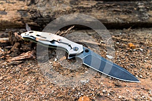 Tactical knife with a black blade on a background of brown wood.