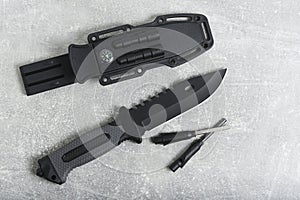 Tactical knife, scabbard and flint with mirror on grey background.