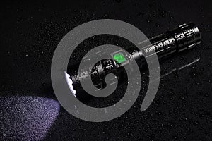 Tactical waterproof flashlight with waterdrops on black background