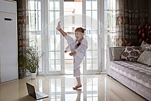 Taekwondo girl in kimono with white belt exercising at home in living room. Online education during coronavirus covid-19 lockdown