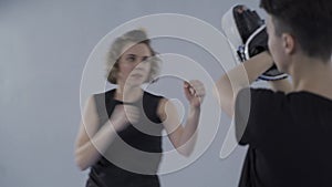 Taekwondo training. Woman practicing hand blows on paws, which is held by trainer. Personal training in taekwondo