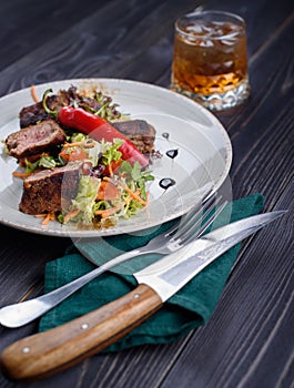 Tagliata of beef with salad on a plate and a glass of whiskey