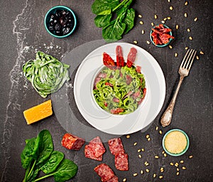 Tagliatelle Pasta with spinach, salami sausage and sun dried tomatoes and Pine nut, fresh basil leaves in white plate