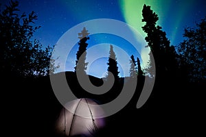 Taiga tent illuminated under northern lights flare