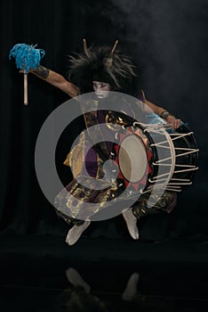 Taiko drummer in demon stage costume and make up junps with drum on stage
