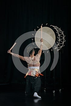 Taiko drummer hits the big drum on stage, back view