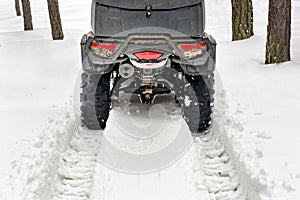 Tail of ATV 4wd quad bike in forest at winter. 4wd all-terreain vehicle stand in heavy snow with deep wheel track. Seasonal